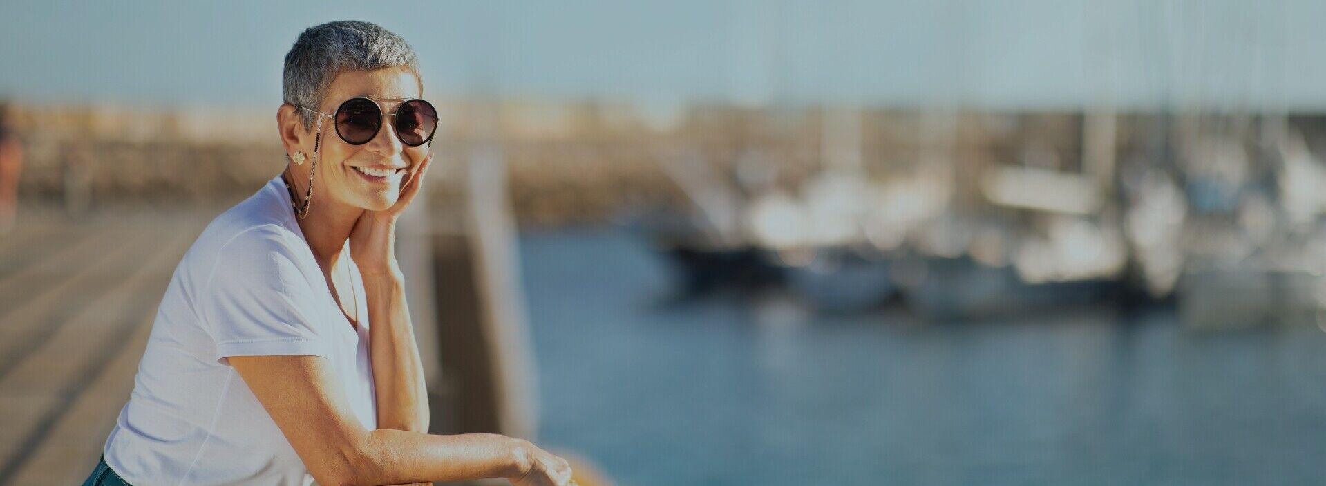 Lächelnde Frau mit Sonnenbrille am Steg mit Booten