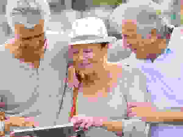 Zwei Männer und zwei Frauen, Arm in Arm, gucken sich etwas auf einem Tablet an