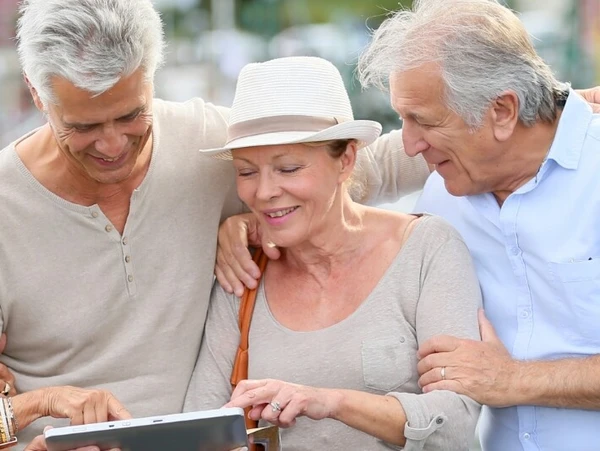 Zwei Männer und zwei Frauen, Arm in Arm, gucken sich etwas auf einem Tablet an